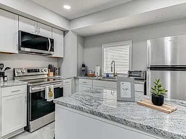 A ground-floor apartment kitchen with white shaker cabinets, granite counters, stainless appliances, and a round breakfast table