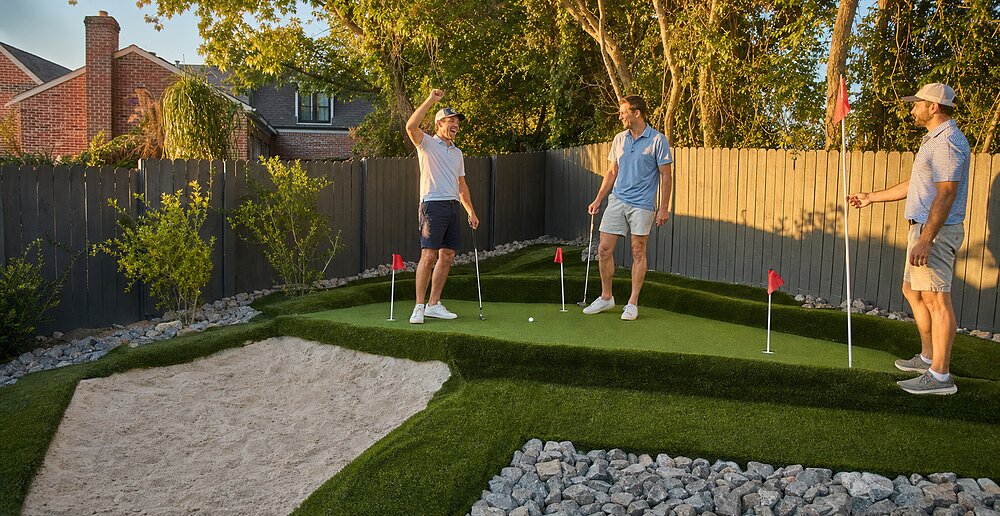 Three friends celebrating a putt on the private putting green at golden hour